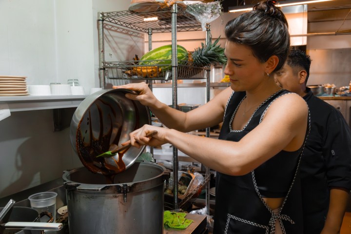 Person pouring sauce into a pot in a kitchen.